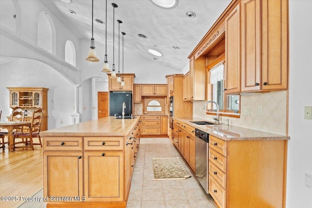 kitchen with sink, black fridge, hanging light fixtures, stainless steel dishwasher, and a kitchen island with sink