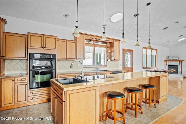 kitchen featuring sink, black appliances, hanging light fixtures, and a center island with sink