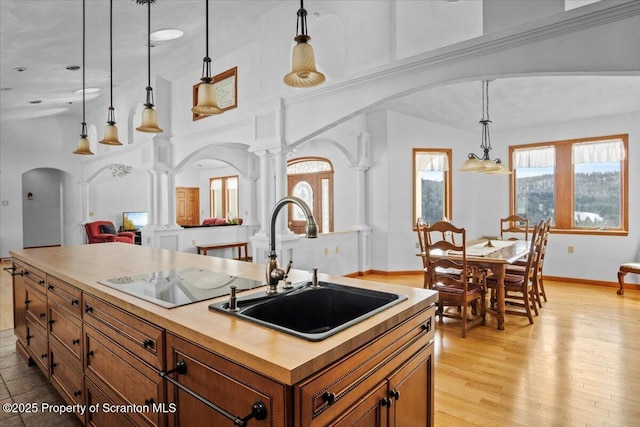 kitchen with decorative light fixtures, decorative columns, sink, a center island with sink, and light wood-type flooring