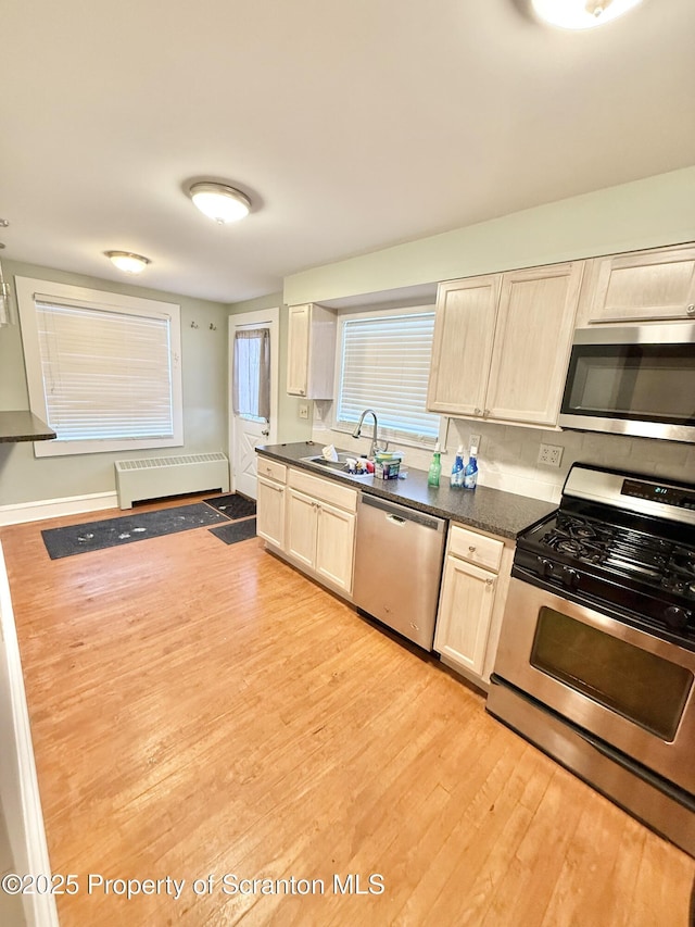 kitchen with light hardwood / wood-style floors, sink, radiator heating unit, and stainless steel appliances