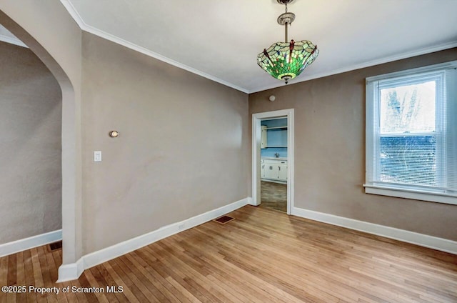 empty room with arched walkways, crown molding, baseboards, and hardwood / wood-style flooring