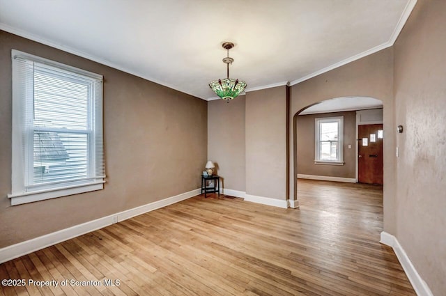 unfurnished dining area with arched walkways, baseboards, crown molding, and light wood-style floors