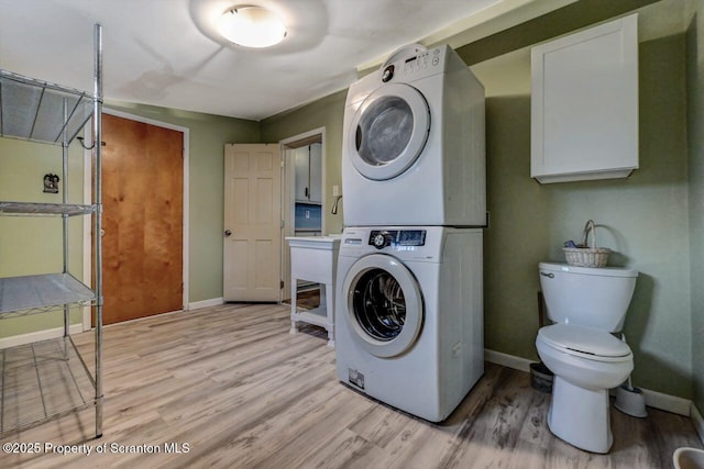 clothes washing area featuring light wood finished floors, laundry area, stacked washer and clothes dryer, and baseboards