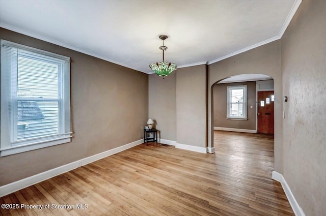 unfurnished dining area with crown molding, light wood-style floors, and arched walkways