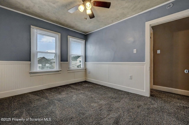 carpeted empty room featuring a ceiling fan, a wainscoted wall, and ornamental molding