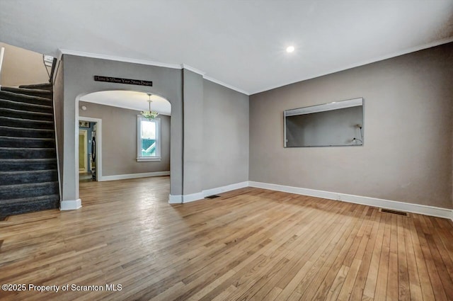 unfurnished room with stairway, arched walkways, wood-type flooring, crown molding, and baseboards