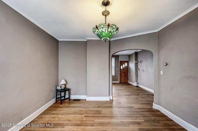unfurnished room featuring crown molding, wood finished floors, arched walkways, and baseboards