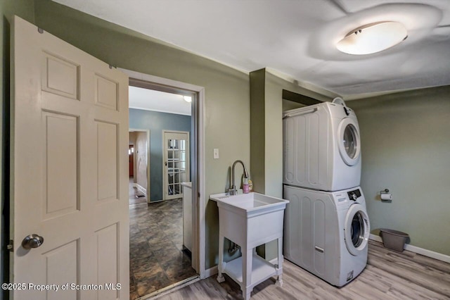 laundry area featuring baseboards, light wood-style floors, stacked washer and clothes dryer, and laundry area