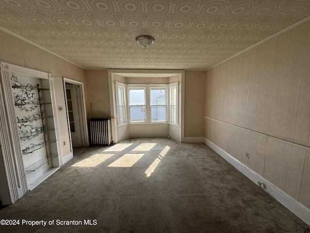 carpeted empty room with wood walls, crown molding, and radiator