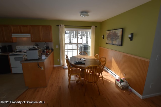 dining space featuring a baseboard heating unit, wainscoting, and light wood-style flooring