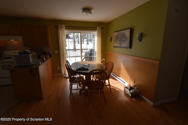 dining space with a wainscoted wall, light wood finished floors, and baseboard heating