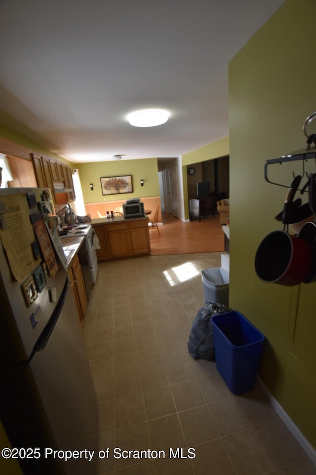 kitchen with brown cabinets, freestanding refrigerator, a peninsula, light countertops, and light tile patterned flooring