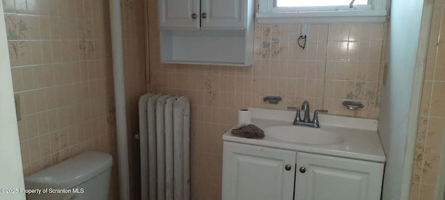 bathroom with tile walls, radiator, vanity, and toilet