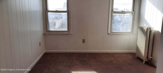 unfurnished room with a healthy amount of sunlight, radiator heating unit, and dark colored carpet