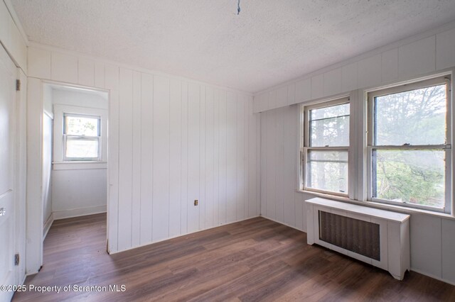 empty room with a textured ceiling, a healthy amount of sunlight, radiator heating unit, and wood finished floors