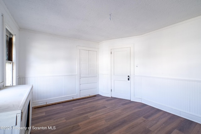 unfurnished room featuring dark wood-type flooring, a textured ceiling, and wainscoting