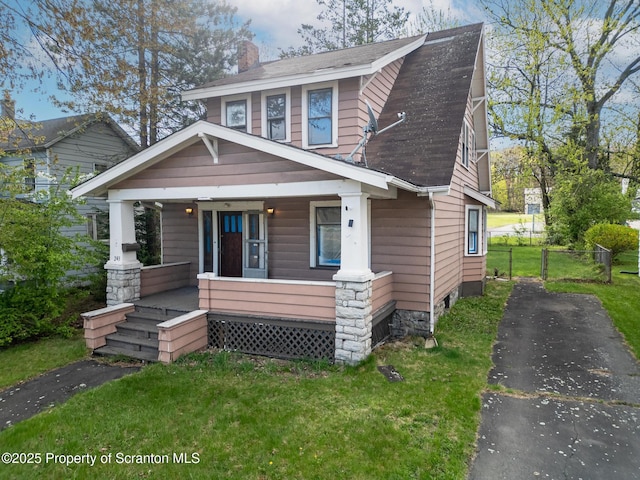 view of front facade featuring a front yard, fence, covered porch, and a chimney