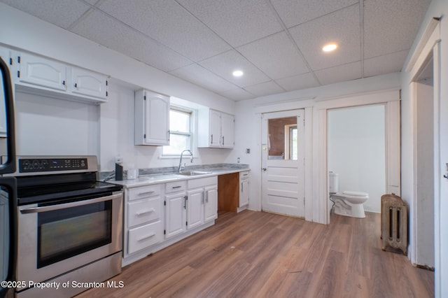 kitchen featuring a sink, light countertops, stainless steel electric stove, radiator, and white cabinetry