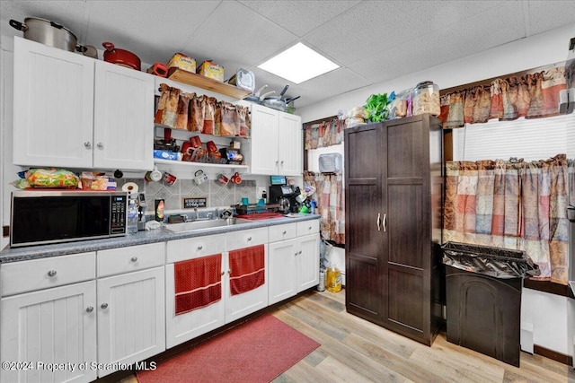 kitchen featuring a paneled ceiling, tasteful backsplash, sink, white cabinets, and light hardwood / wood-style floors