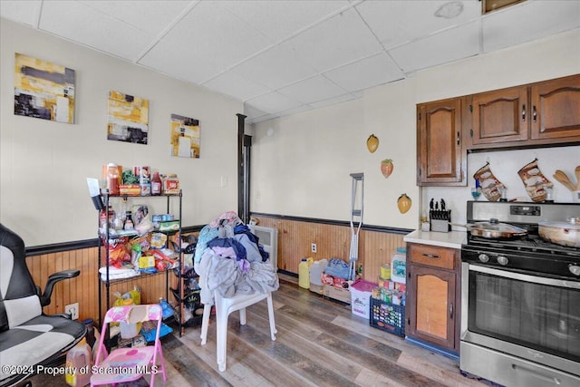 kitchen featuring wood-type flooring, stainless steel stove, a drop ceiling, and wooden walls