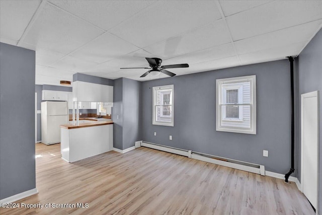 unfurnished living room featuring a paneled ceiling, ceiling fan, light wood-type flooring, and a baseboard heating unit