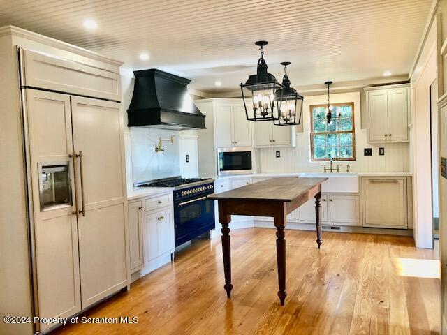 kitchen with premium range hood, white cabinets, light hardwood / wood-style flooring, built in appliances, and a chandelier