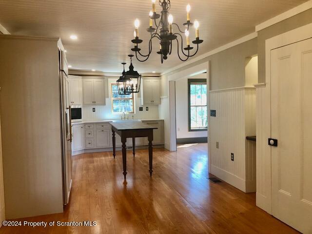 kitchen with pendant lighting, an inviting chandelier, white cabinets, crown molding, and light hardwood / wood-style flooring