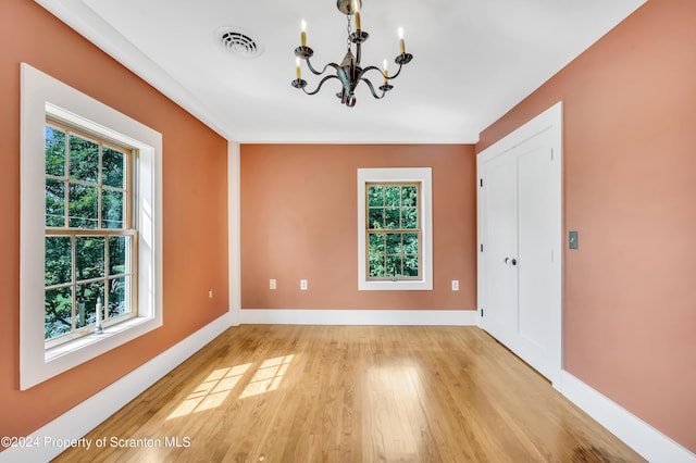 empty room featuring a chandelier, a healthy amount of sunlight, and light wood-type flooring