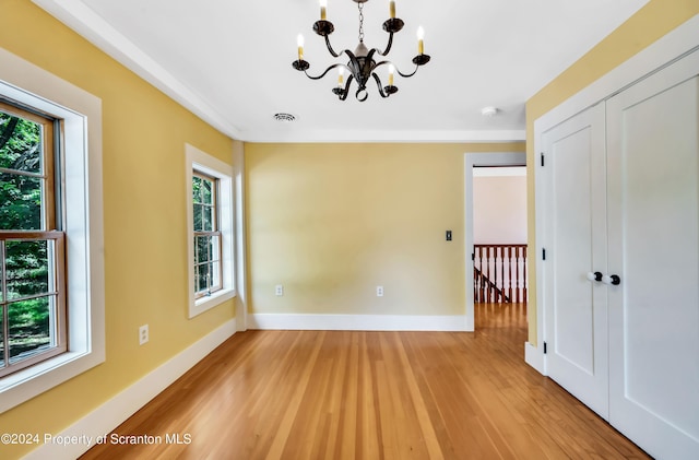 unfurnished room with a healthy amount of sunlight, wood-type flooring, and an inviting chandelier