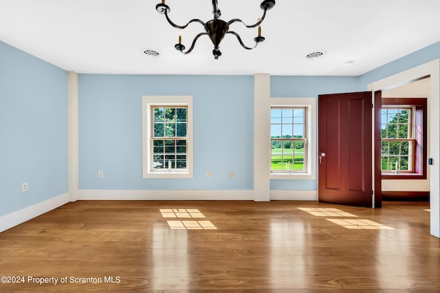 unfurnished room featuring a chandelier, light wood-type flooring, and a healthy amount of sunlight