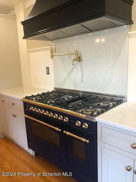 kitchen with premium range hood, light hardwood / wood-style flooring, white cabinets, and double oven range