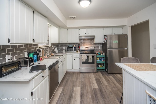 kitchen with appliances with stainless steel finishes, sink, white cabinets, decorative backsplash, and hardwood / wood-style flooring