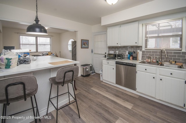 kitchen with sink, hardwood / wood-style floors, white cabinets, decorative light fixtures, and stainless steel dishwasher