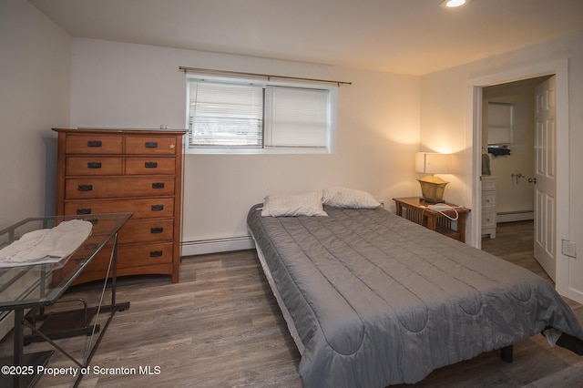 bedroom featuring dark hardwood / wood-style flooring, a baseboard heating unit, and ensuite bathroom