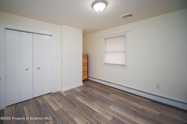 unfurnished bedroom featuring wood-type flooring, a baseboard heating unit, and a closet