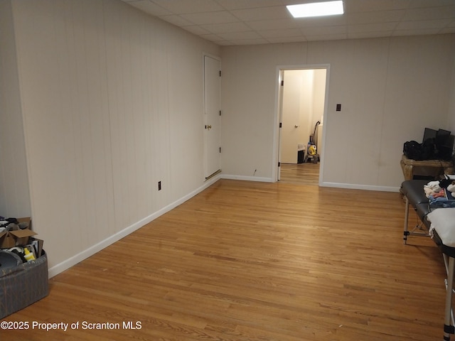 unfurnished room with light wood finished floors, a paneled ceiling, and baseboards