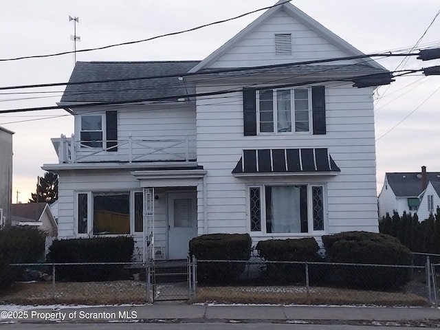 view of front of house with a balcony, a gate, a standing seam roof, a shingled roof, and a fenced front yard