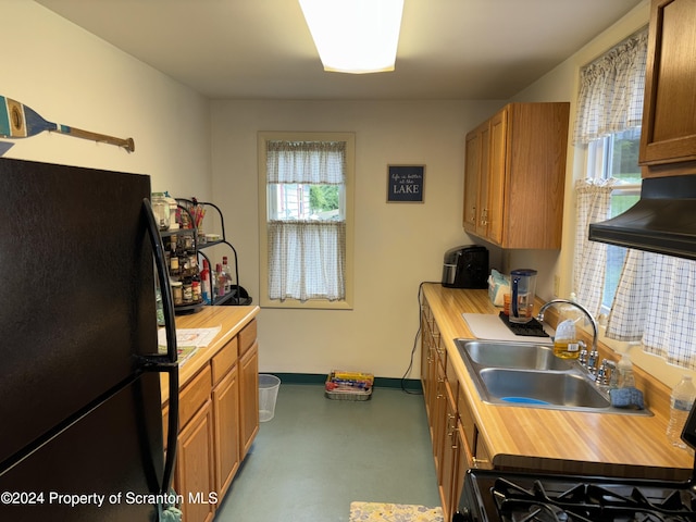 kitchen with stove, black fridge, sink, concrete floors, and range hood