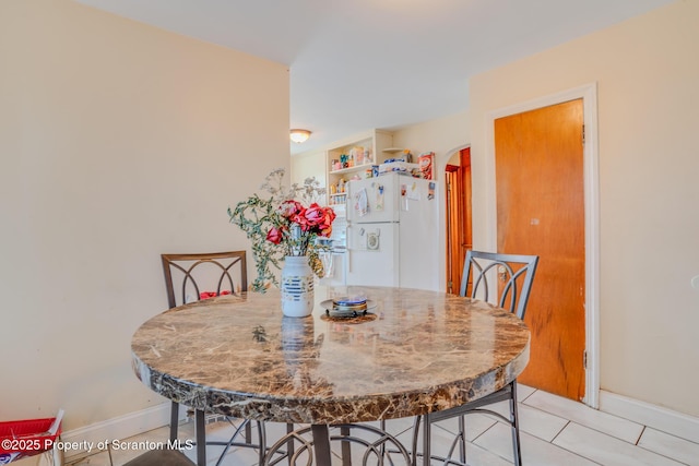 dining space featuring baseboards, arched walkways, and tile patterned flooring