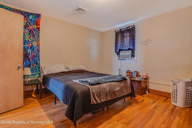 bedroom with light wood-style floors, baseboards, cooling unit, and visible vents