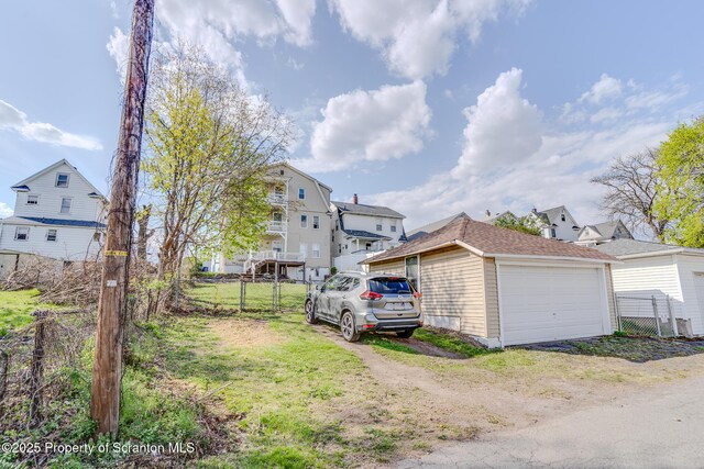 view of side of home with a detached garage, fence, a residential view, and an outdoor structure