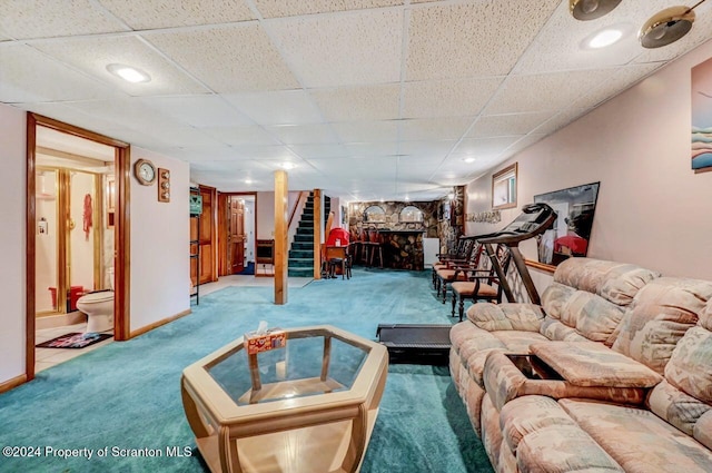 living room with carpet flooring, a drop ceiling, and a stone fireplace