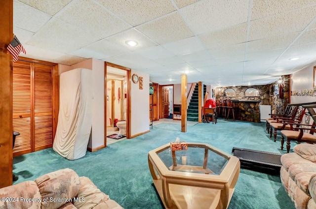 carpeted living room featuring a paneled ceiling and a stone fireplace