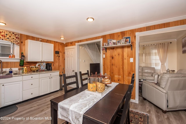 dining area featuring light wood-type flooring, wooden walls, ornamental molding, and sink