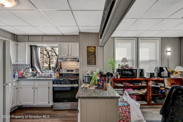 kitchen with dark wood-type flooring, freestanding refrigerator, black microwave, under cabinet range hood, and stainless steel gas range oven