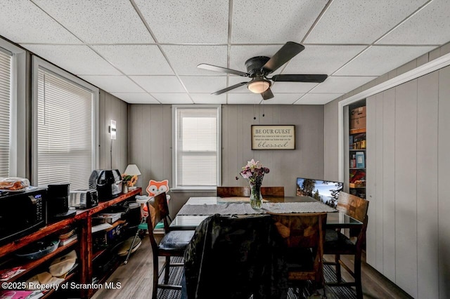 dining area with a ceiling fan, a drop ceiling, and wood finished floors