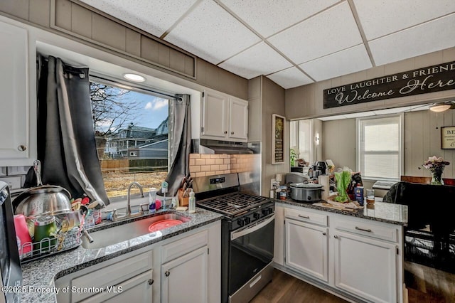 kitchen with backsplash, white cabinets, a sink, under cabinet range hood, and stainless steel gas range oven