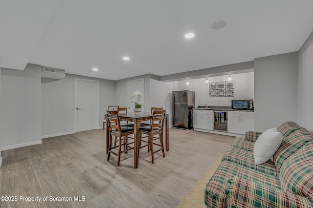 dining area with light wood-type flooring, beverage cooler, and bar area