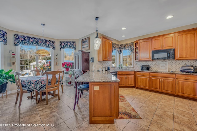 kitchen with light stone countertops, a healthy amount of sunlight, a kitchen bar, and decorative light fixtures