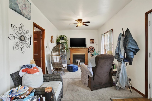 living area featuring a ceiling fan, a glass covered fireplace, and carpet